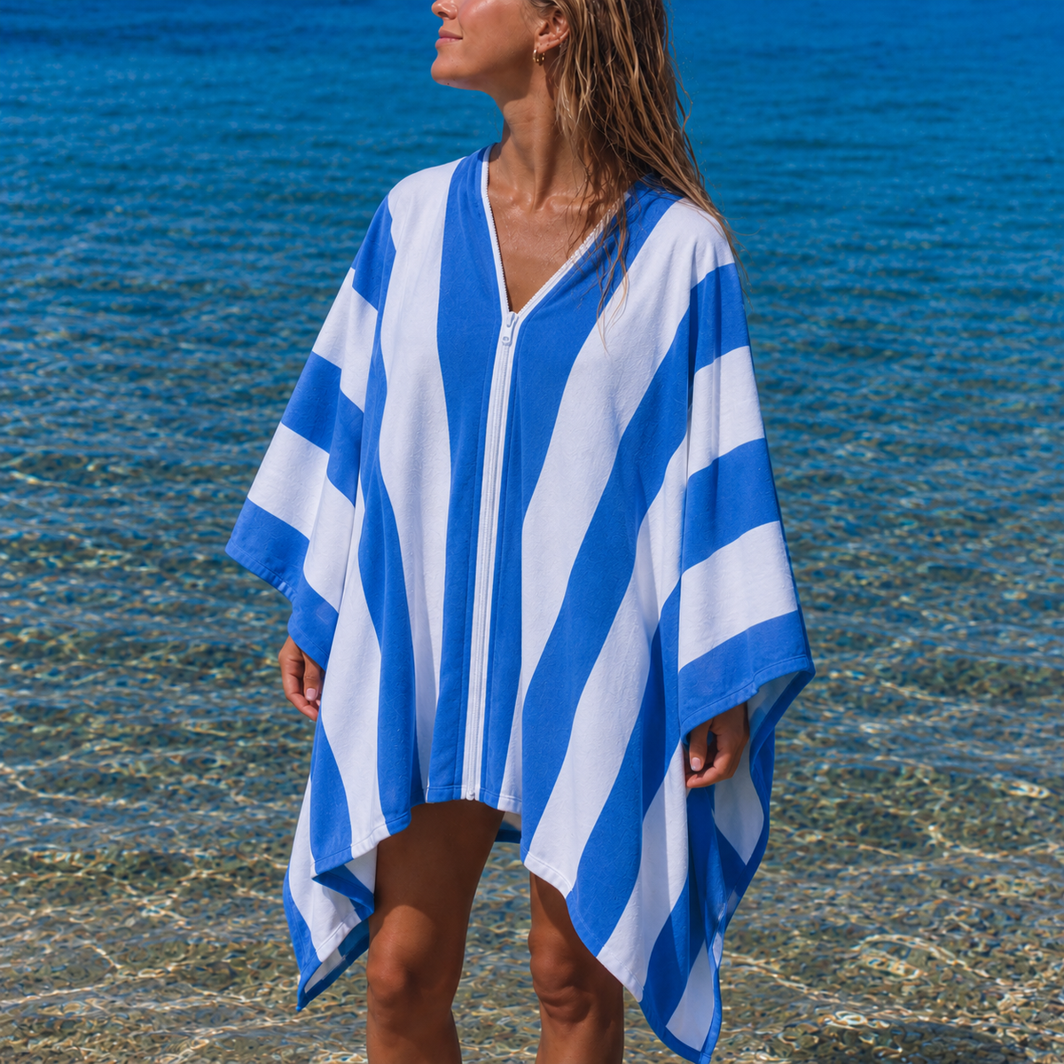 Woman standing in the shallows wearing the zipped Zipp hands-free micro-fibre beach towel in blue and white stripes in Cape Town
