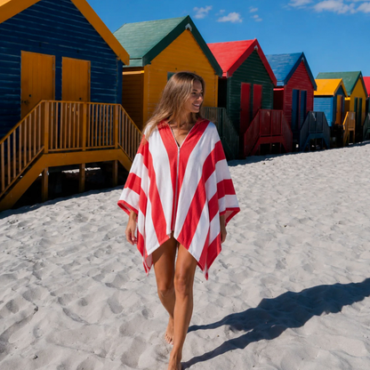 Woman walking past the Muizenberg beach huts wearing the red and white Zippa hands-free microfibre towel, zipped closed and hands free